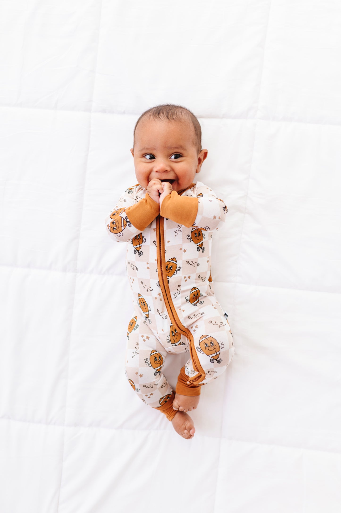 Baby wearing a patterned onesie with a brown strap on a white background
