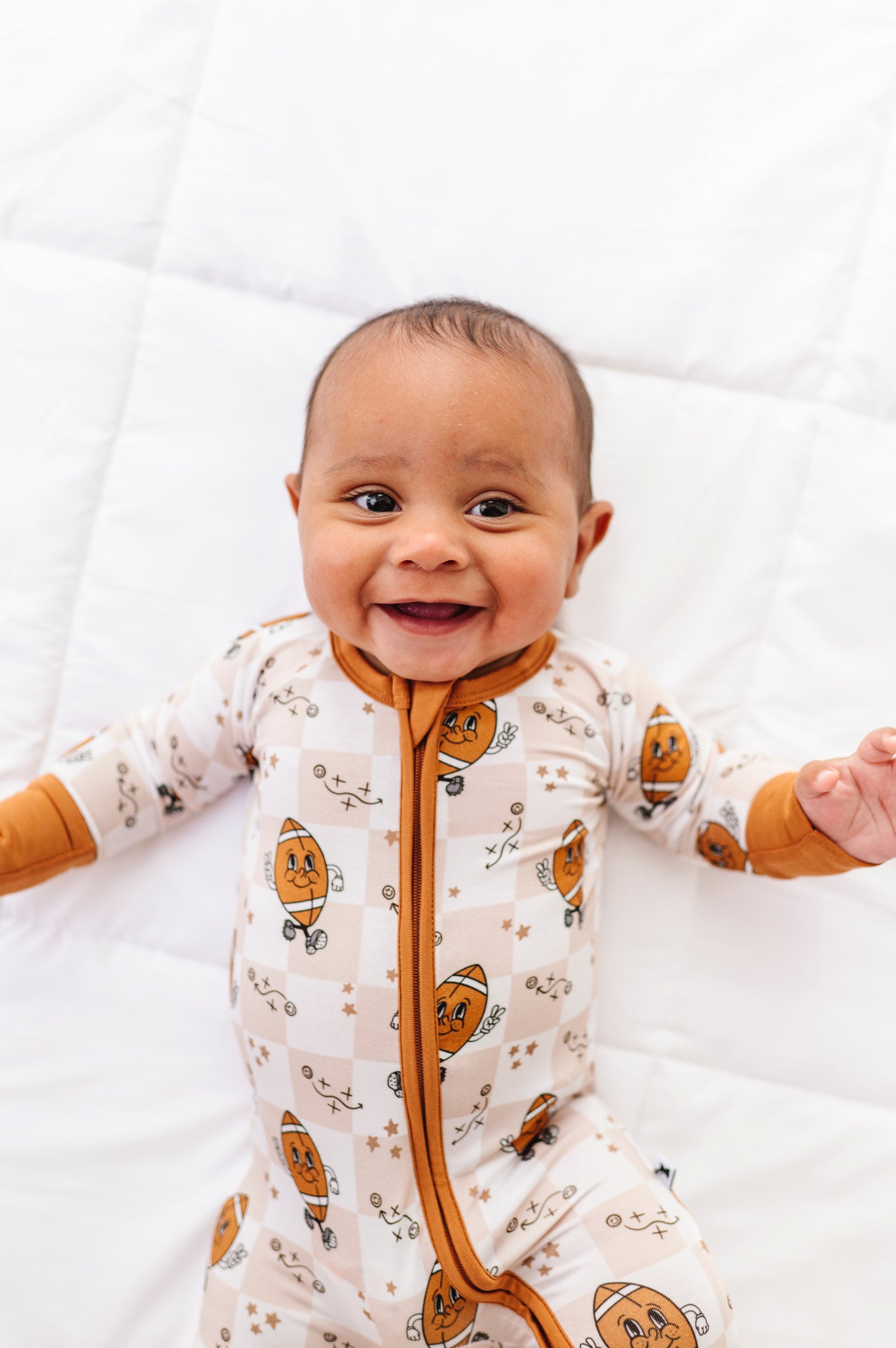 Baby wearing a white onesie with football patterns on a white background