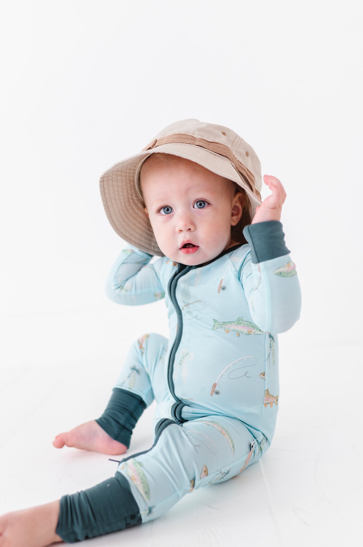 Baby wearing a light blue onesie with animal prints and a beige hat on a white background