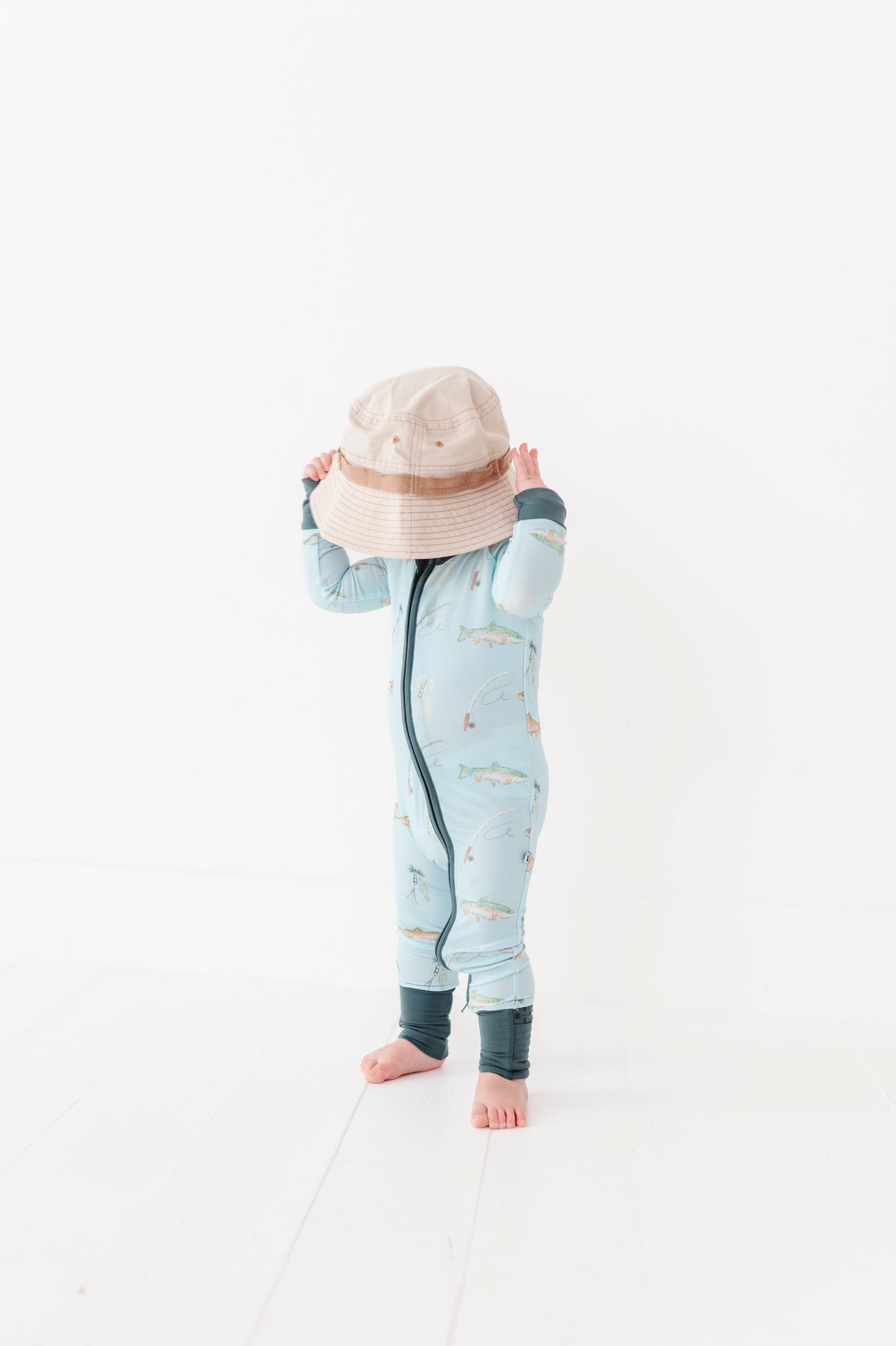 Child wearing a light blue onesie with a pattern, standing on a white background