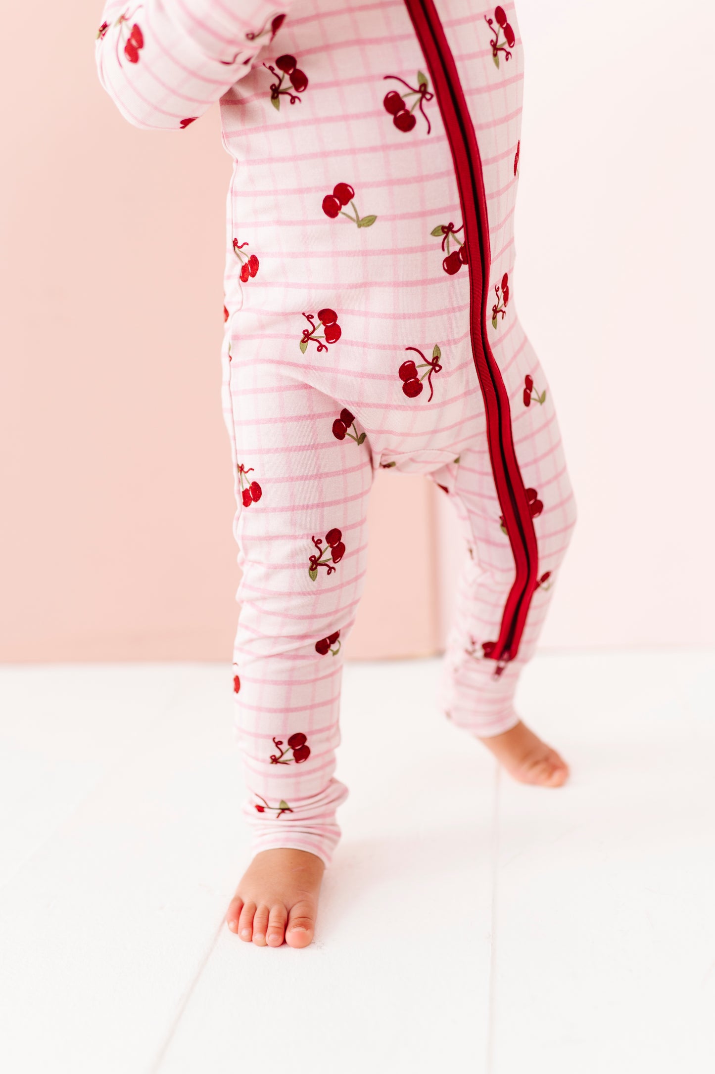 Baby wearing a white onesie with red cherry pattern on a light pink background