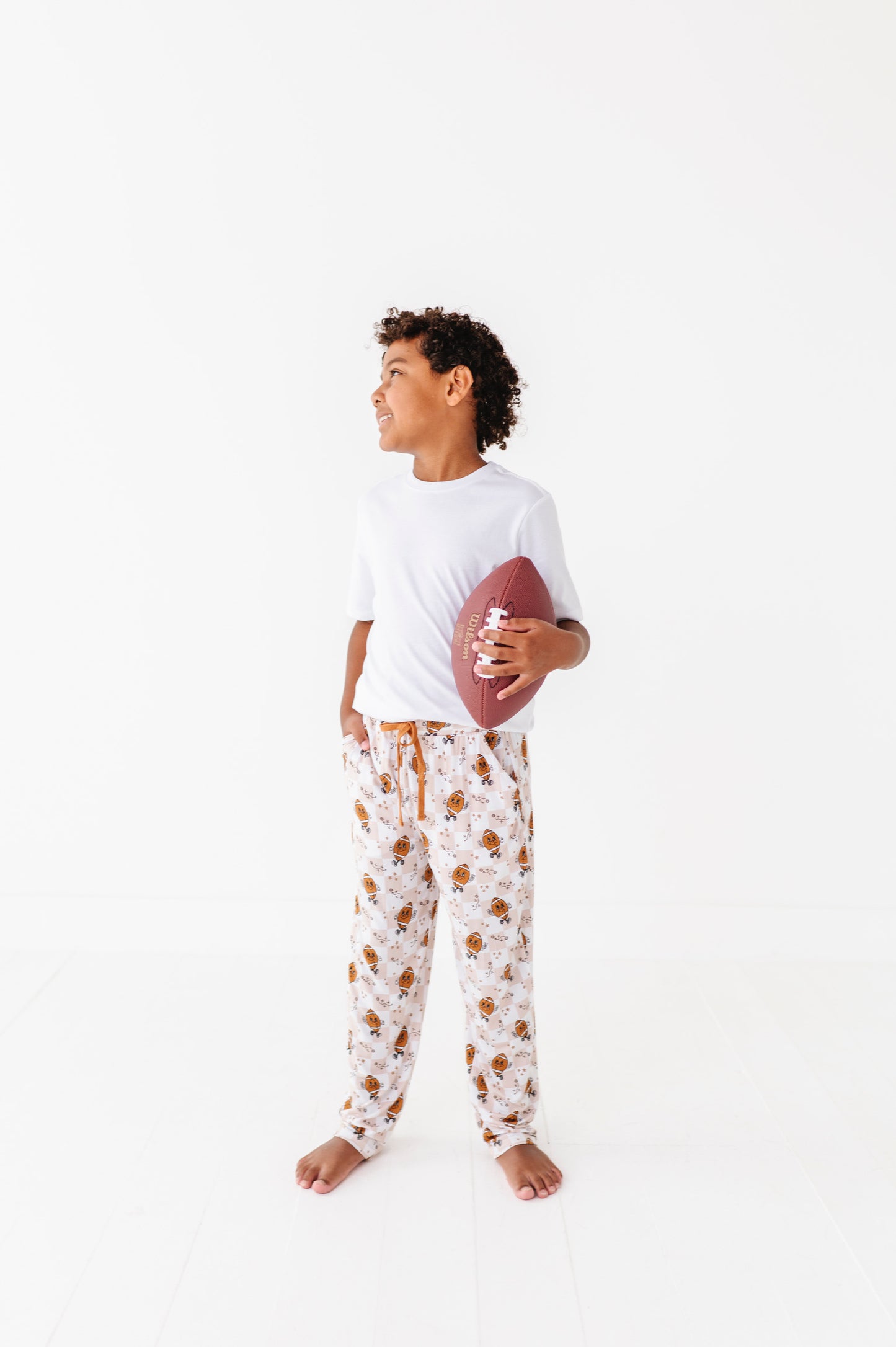 Person wearing a white t-shirt and patterned pajama pants holding a football on a white background