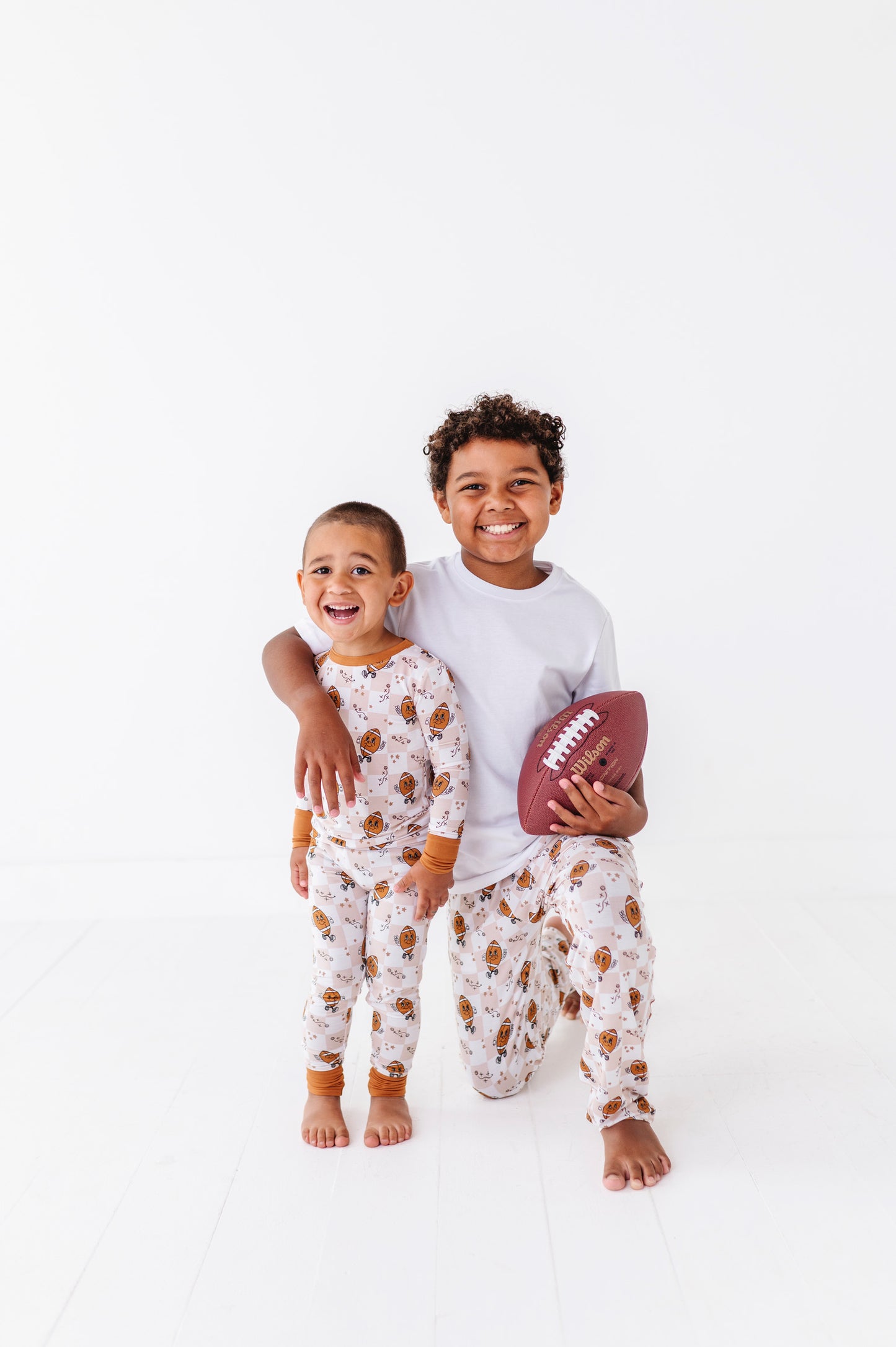 Two children in matching pajamas with one holding a football on a white background
