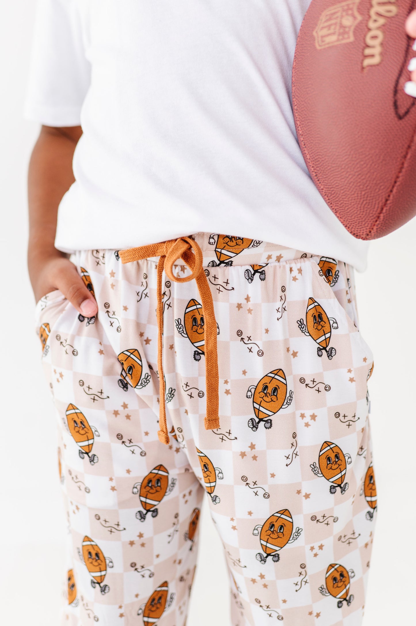Person wearing pajama pants with football pattern holding a football.