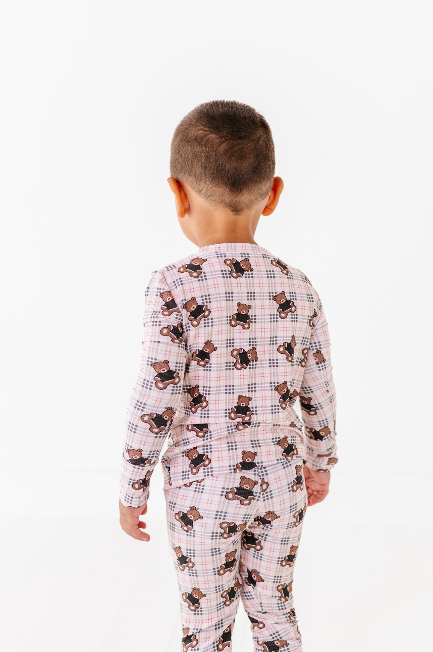 Child wearing a checkered pajama set with teddy bear pattern on a white background
