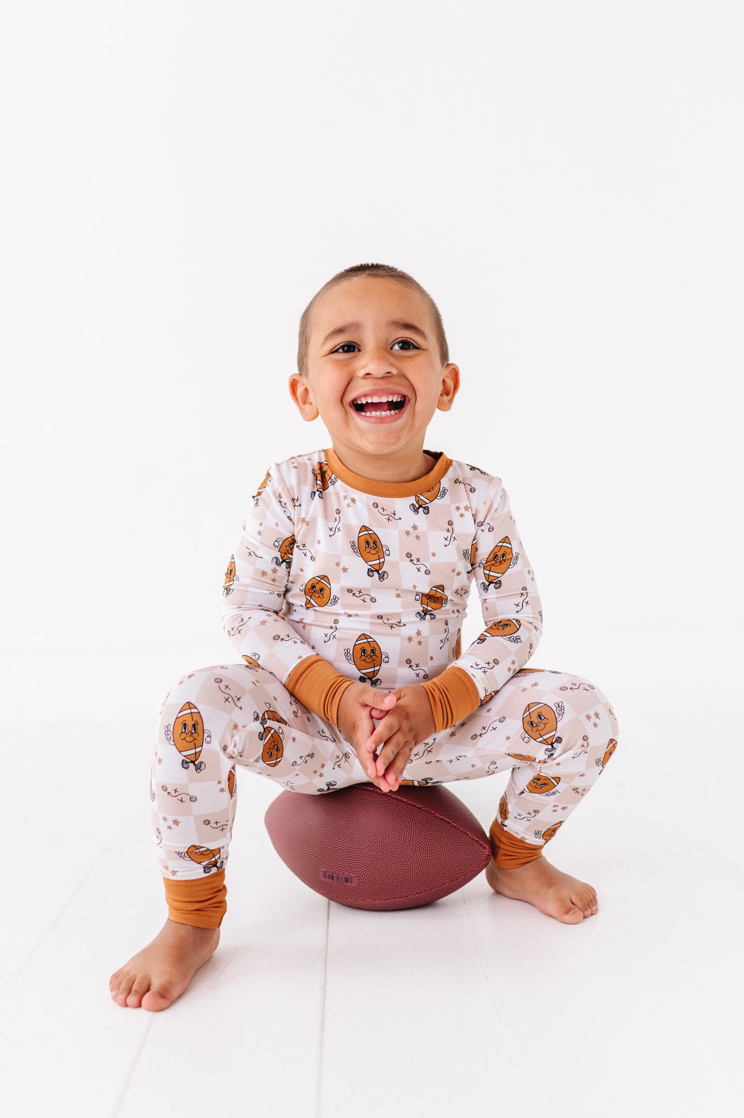Child wearing patterned pajamas sitting on a white floor with a white background