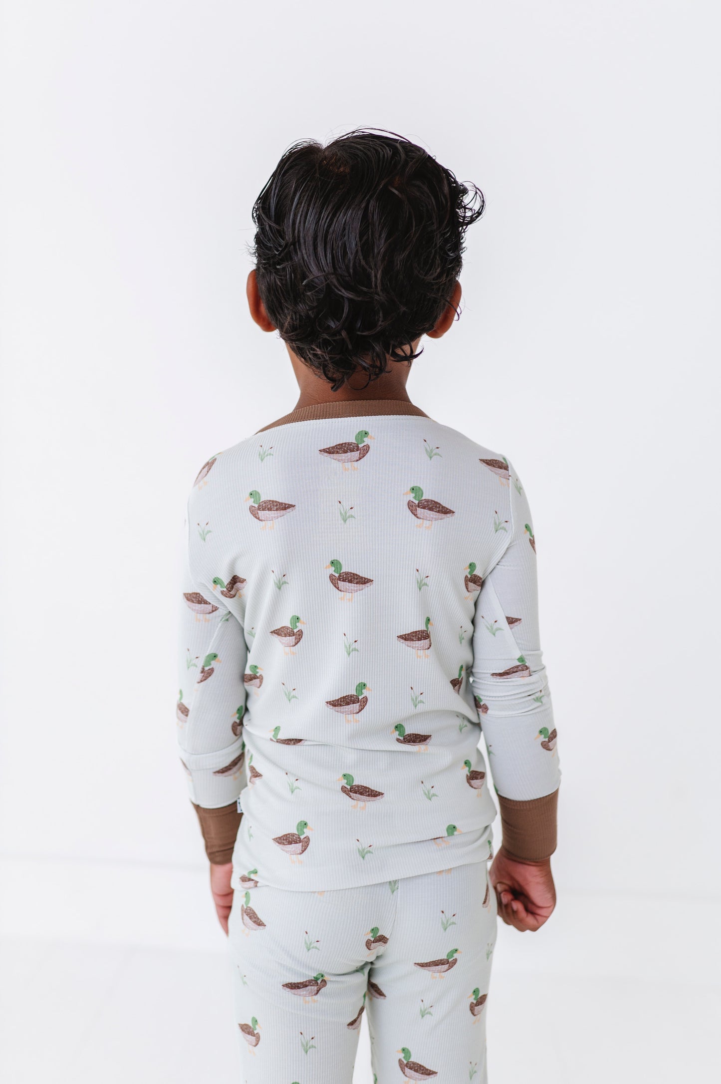 Child wearing a long-sleeve shirt and pants with duck pattern on a white background