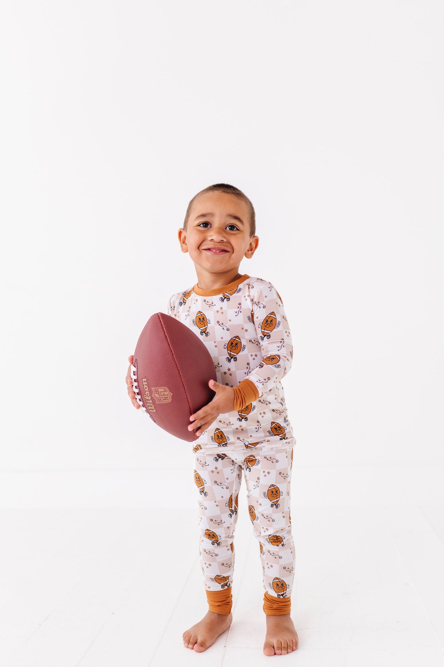 Child wearing pajamas with a football pattern, holding a football on a white background