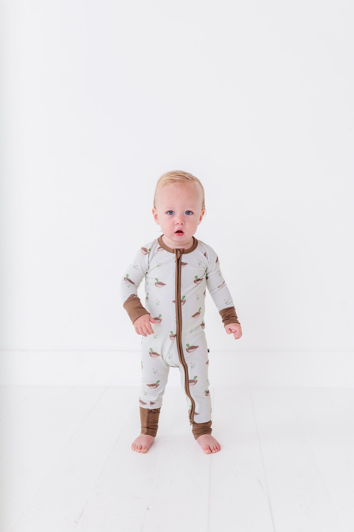 Baby wearing a white onesie with brown accents on a white background