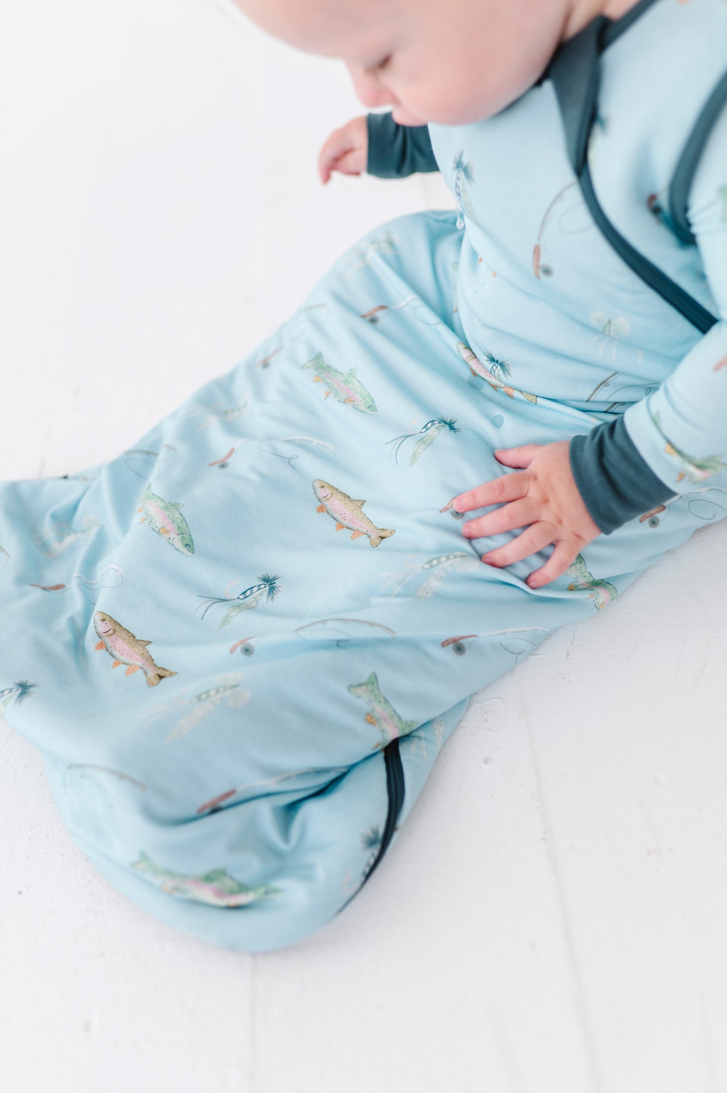 Baby wrapped in a blue swaddle with fish pattern on a white surface