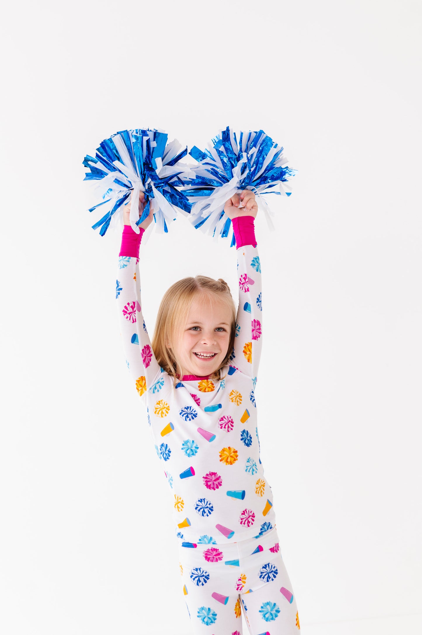 Child wearing colorful pajamas holding blue pom-poms against a white background