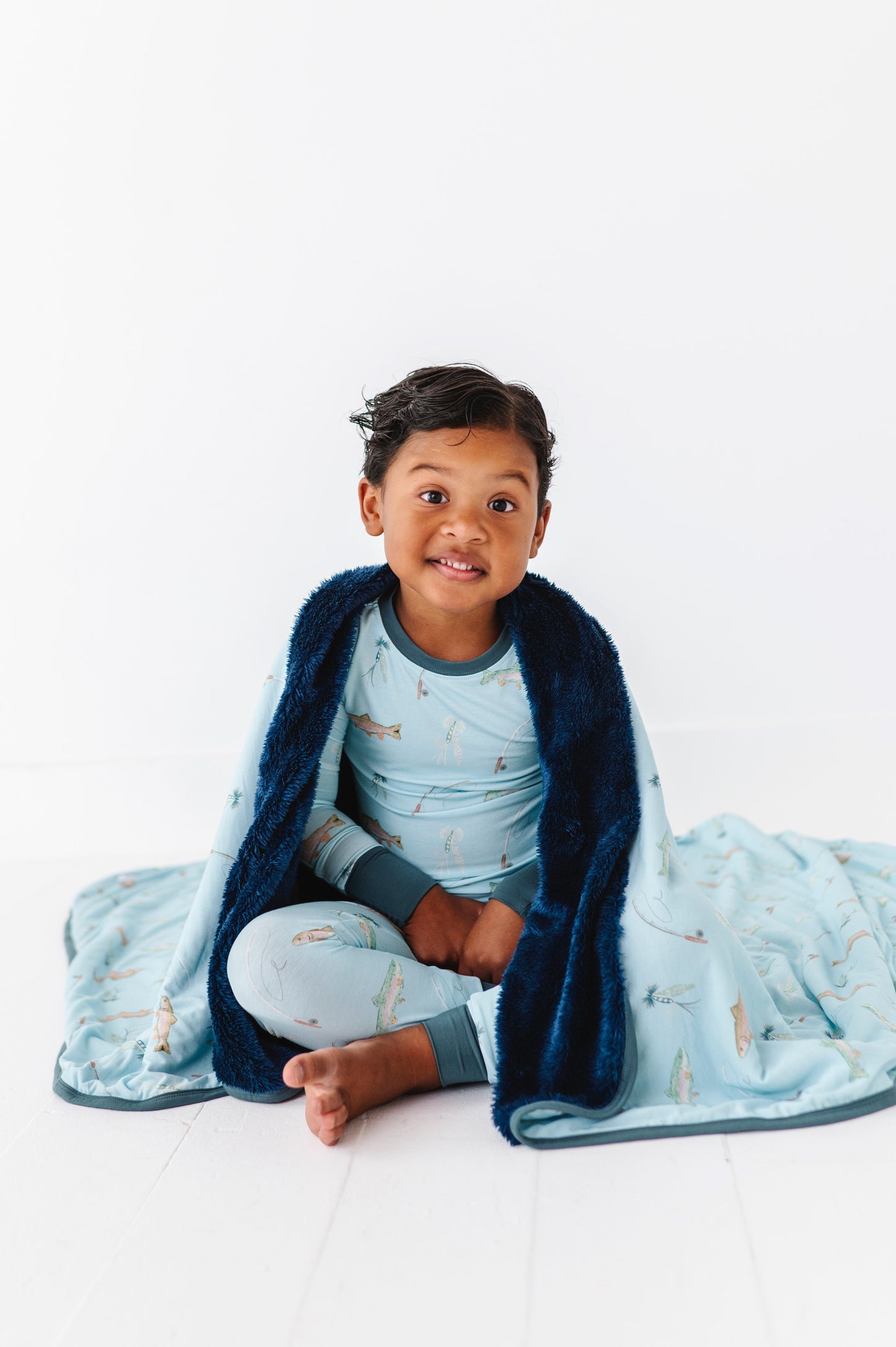 Child wrapped in a blue blanket with fish pattern on a white background