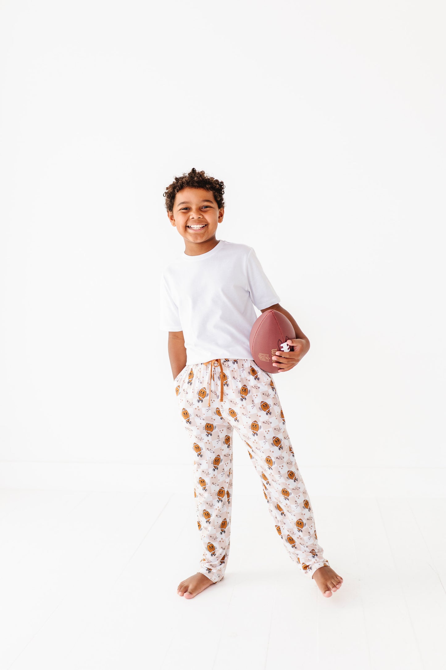 Child wearing a white t-shirt and patterned pajama pants holding a football on a white background