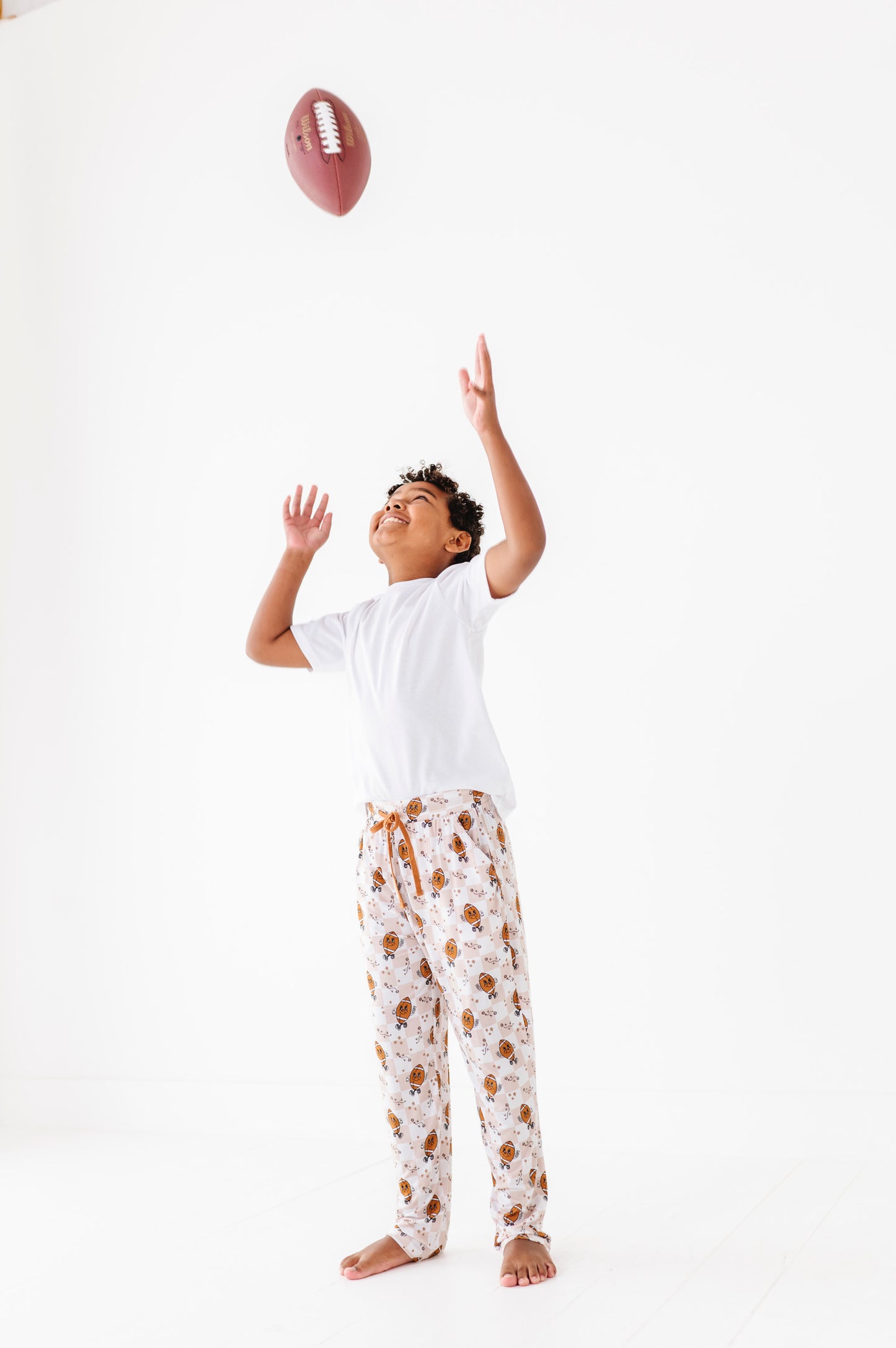 Child in pajama pants reaching up to catch a football on a white background