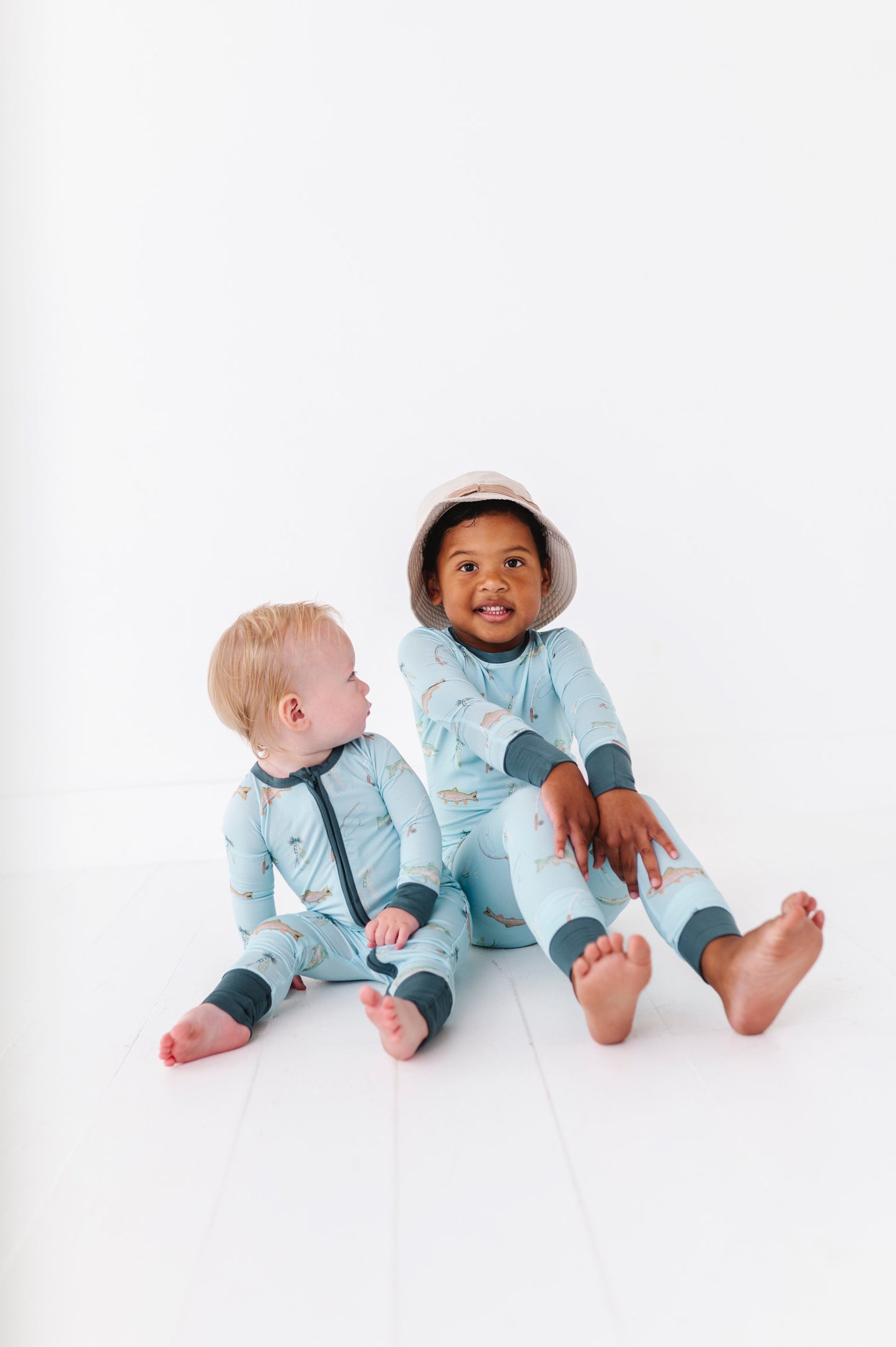 Two children wearing matching blue and fish pajamas sitting on a white background