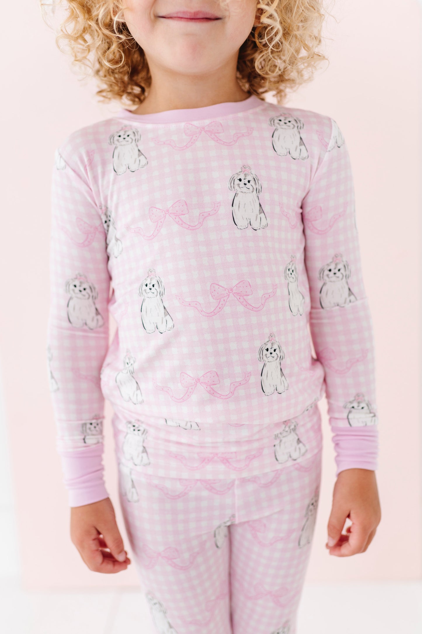 Child wearing pink pajamas withdog pattern on a light pink background