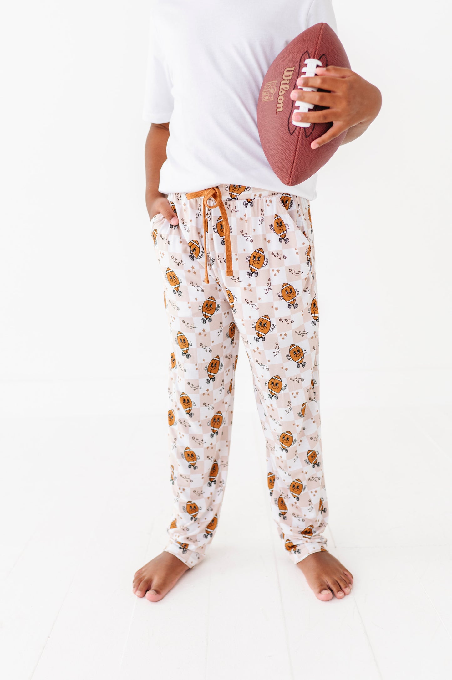 Person wearing patterned pajama pants holding a football on a white background
