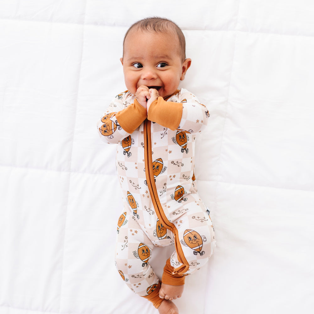 
                      
                        Baby wearing a patterned onesie with a brown strap on a white background
                      
                    