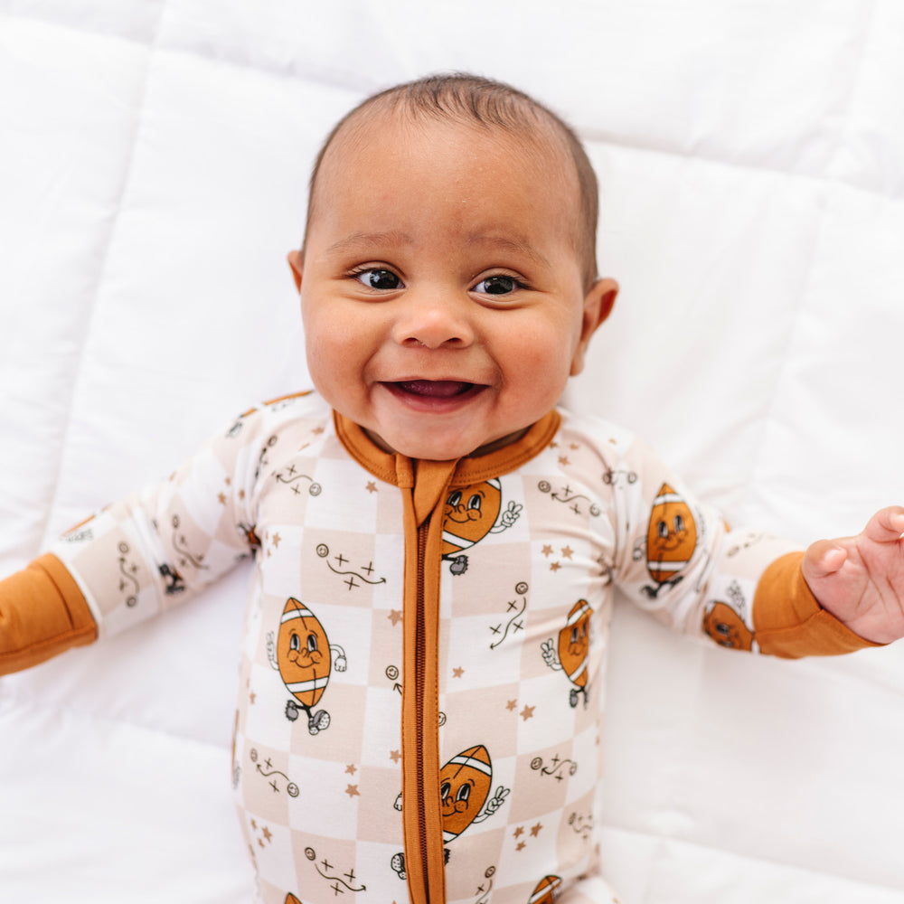 
                      
                        Baby wearing a white onesie with football patterns on a white background
                      
                    