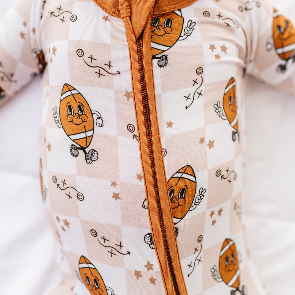 Baby wearing a onesie with football design and brown zipper on a white background