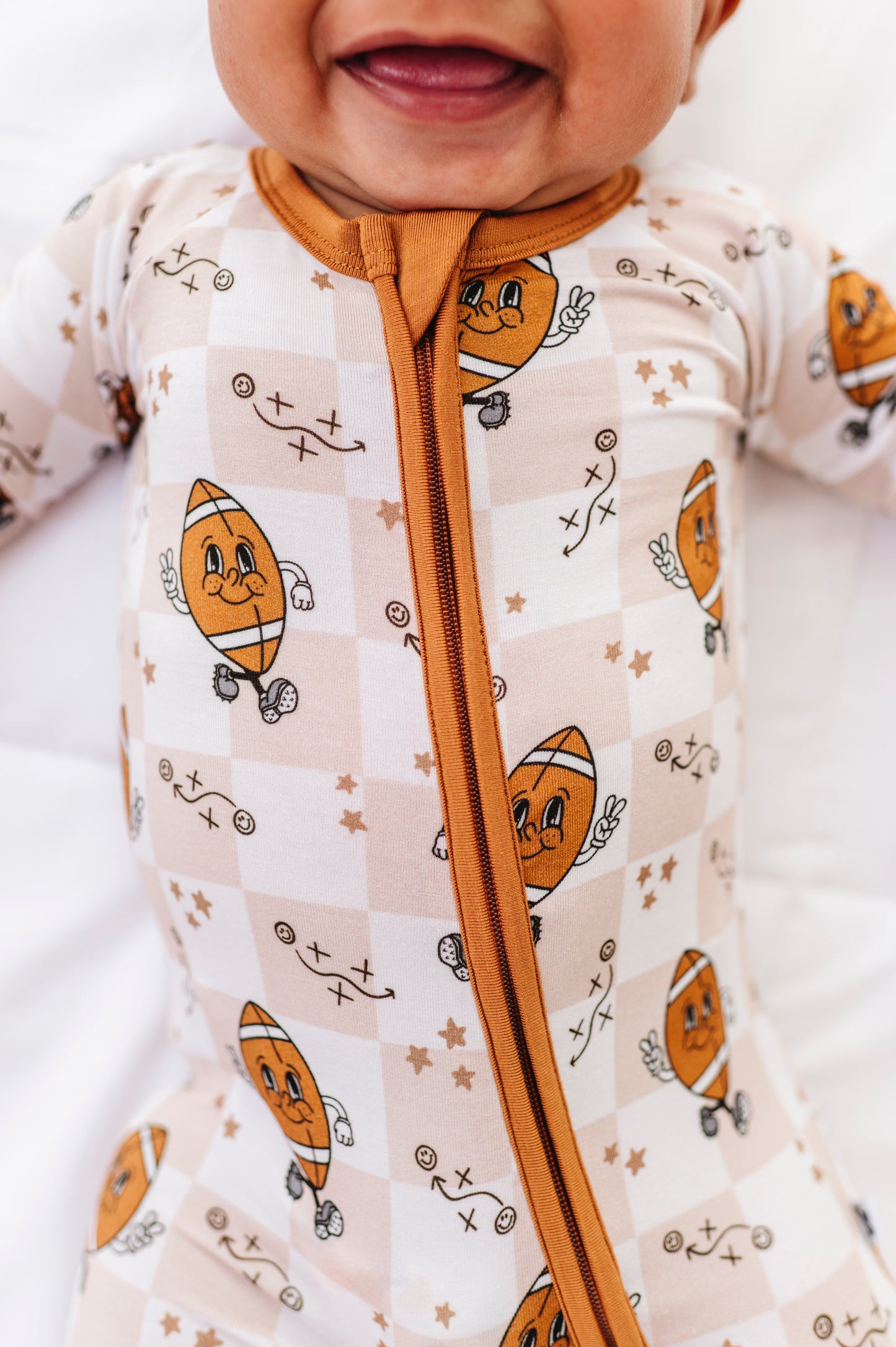 Baby wearing a onesie with football design and brown zipper on a white background