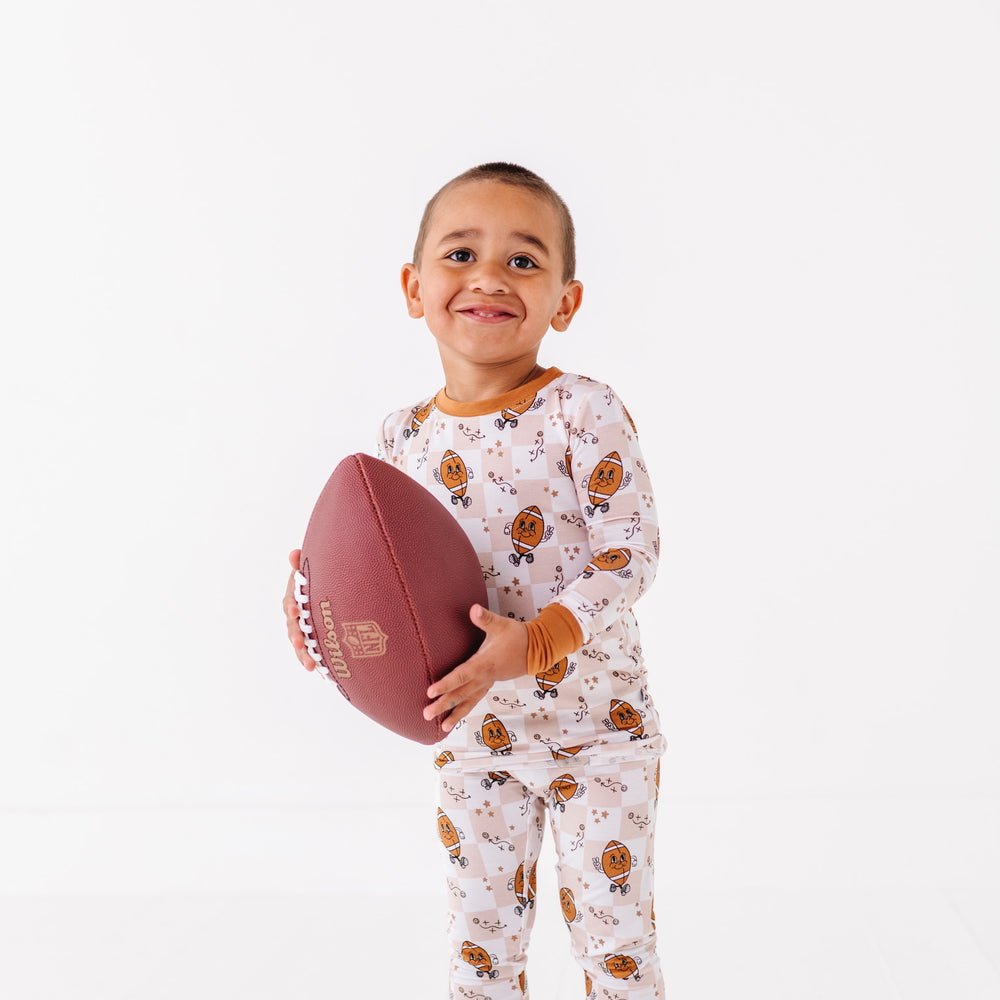 
                      
                        Child wearing pajamas with a football pattern, holding a football on a white background
                      
                    
