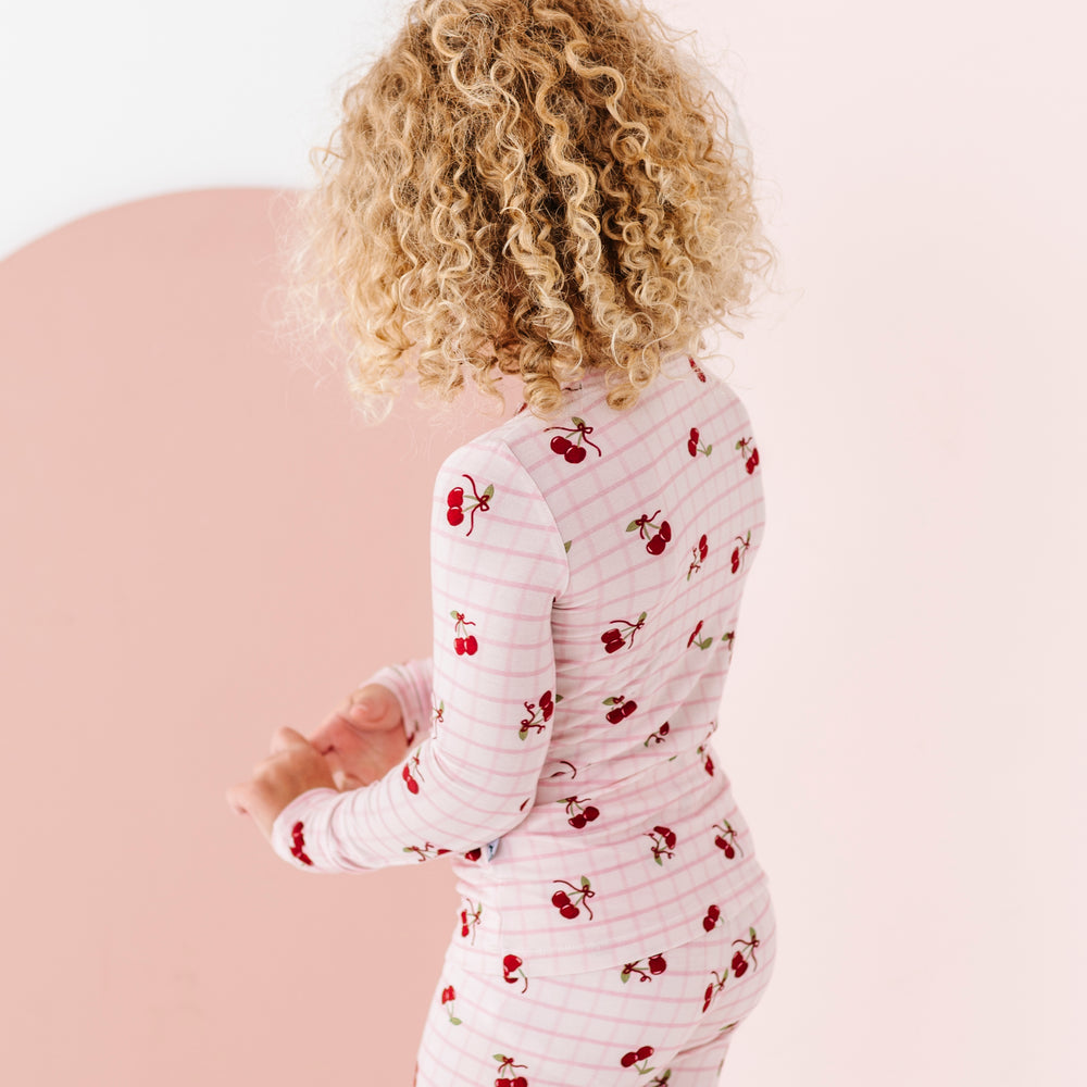
                      
                        Child wearing a white onesie with red cherry pattern on a pink background
                      
                    