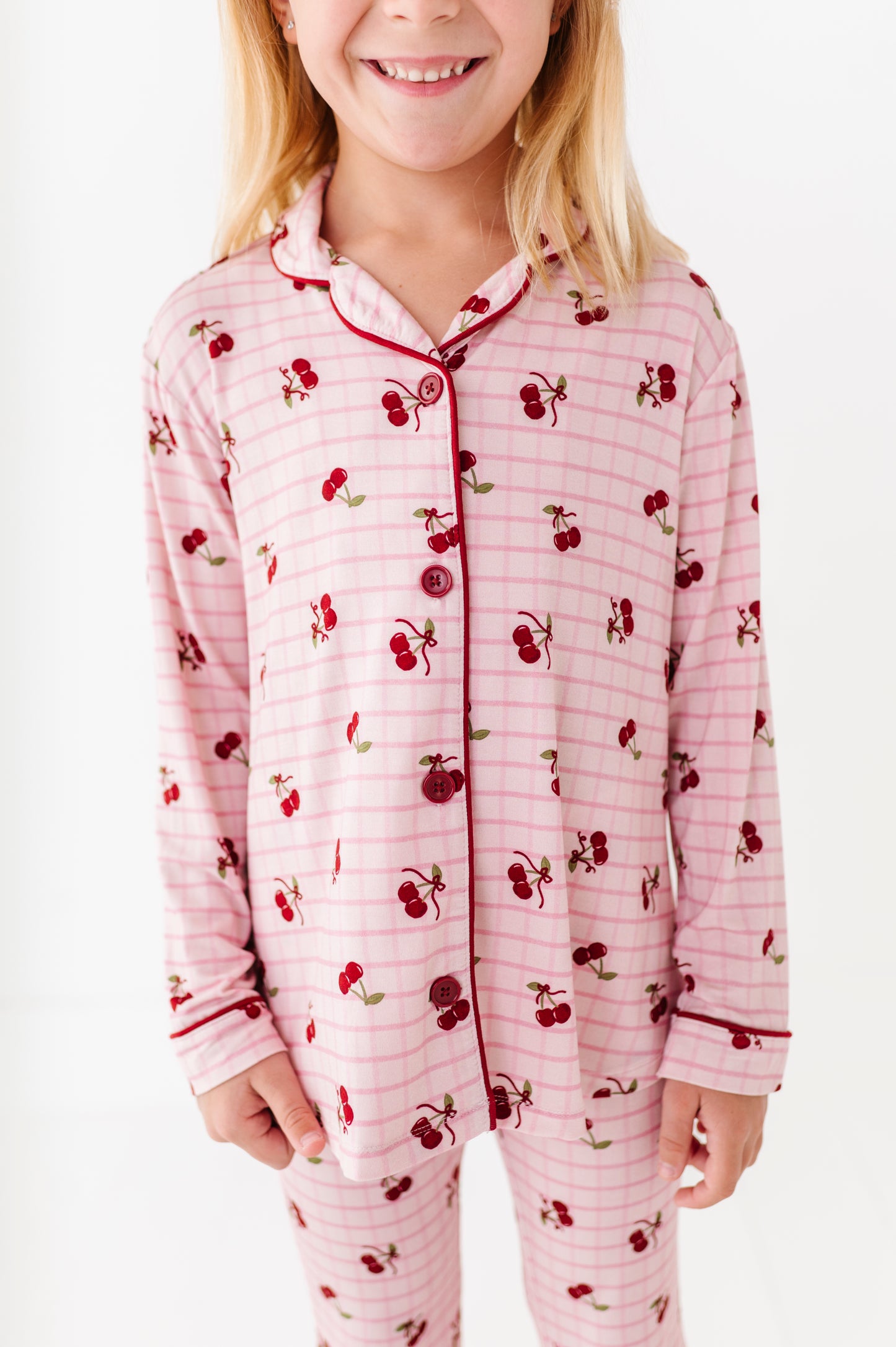 Child wearing a pink pajama set with cherry pattern on a white background