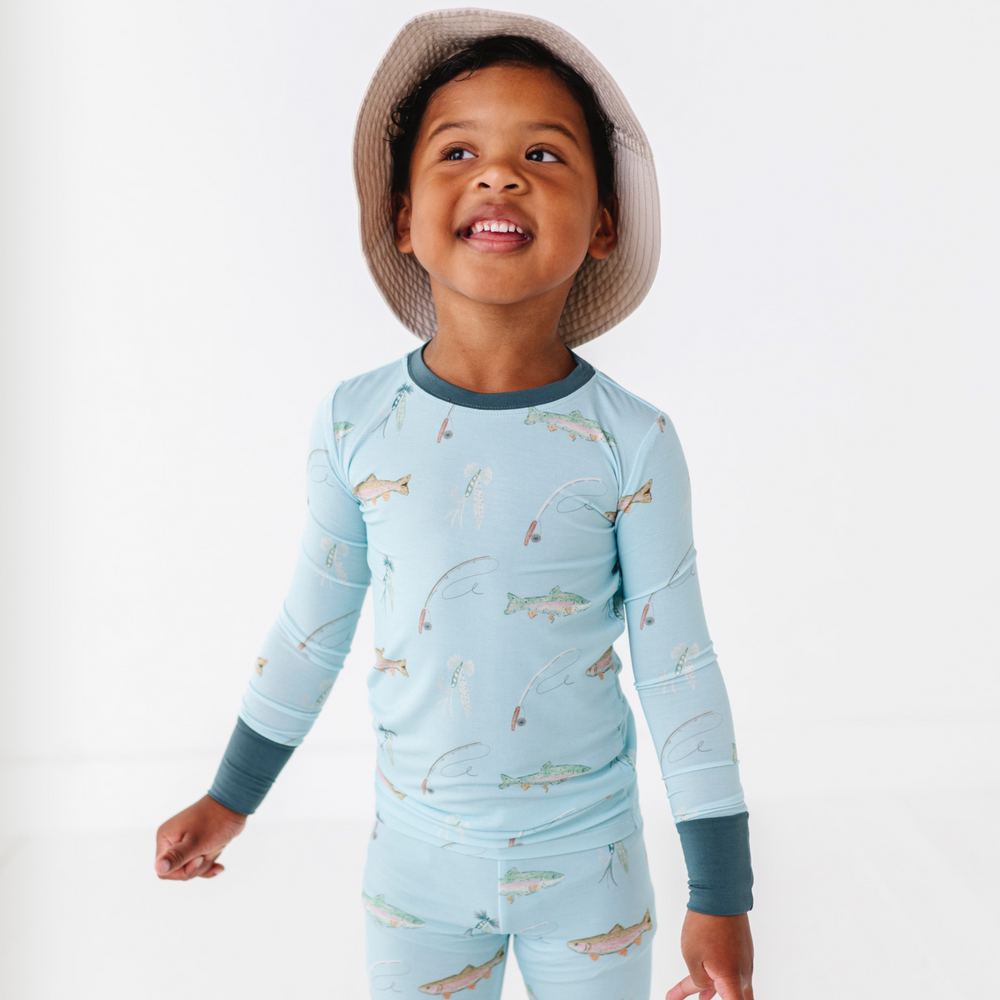 Child wearing a light blue long-sleeve shirt and pants with fish pattern, standing against a white background.