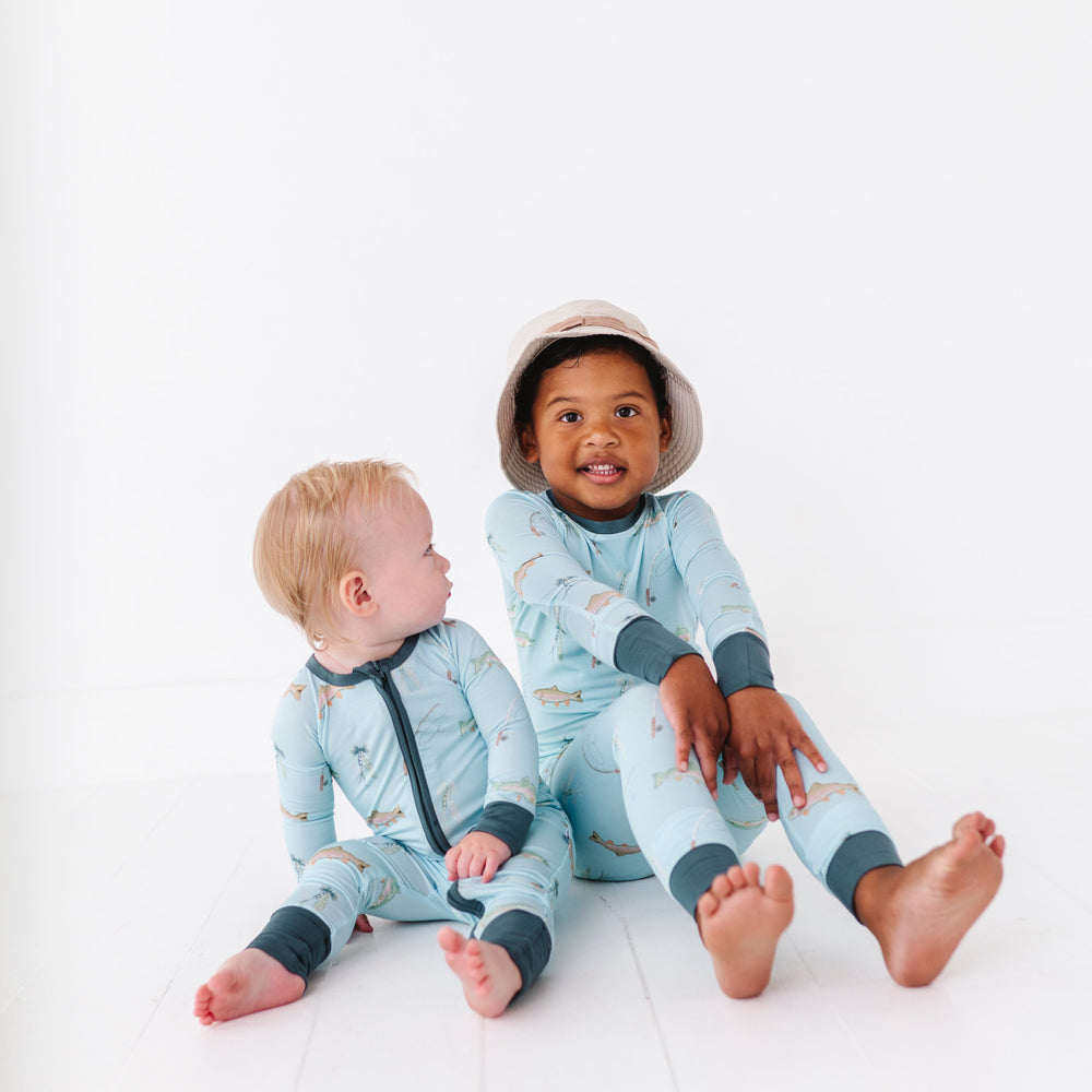
                      
                        Two children wearing matching blue and fish pajamas sitting on a white background
                      
                    